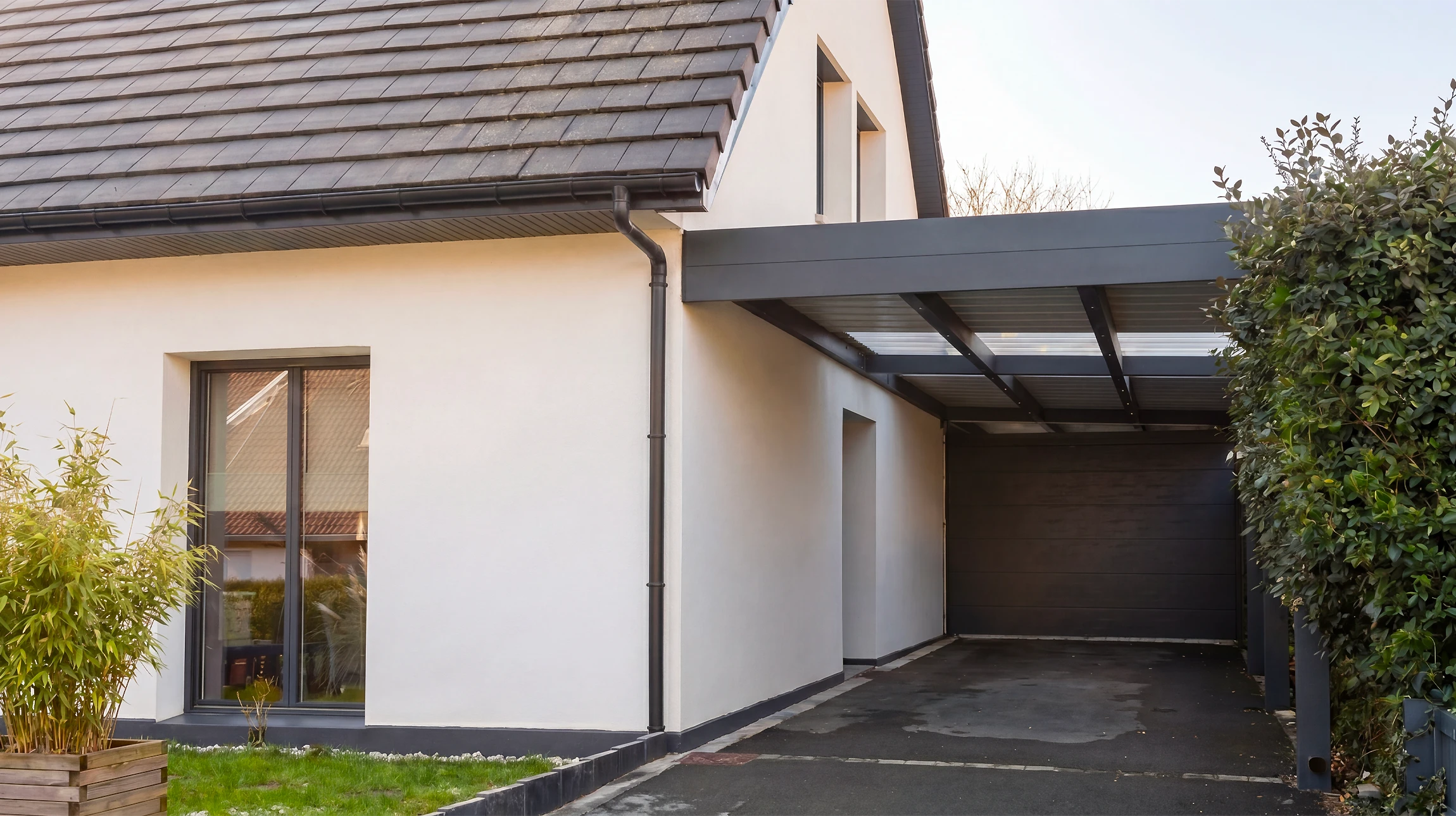 Carport adossé à une maison individuelle moderne, façade enduit blanc, toiture tuiles ardoise