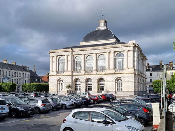 Vue aérienne ou perspective d'une petite ville française de la région des Hauts-de-France montrant l'urbanisme local avec maisons résidentielles traditionnelles et modernes, rues pavées ou routes régionales, points de repère architecturaux locaux comme une église ou bâtiments commerciaux, entourés de zone rurale avec champs ou verdure. La photo doit capturer l'essence géographique et administrative d'une commune picarde, en lumière naturelle claire, sans texte ou overlay visible.